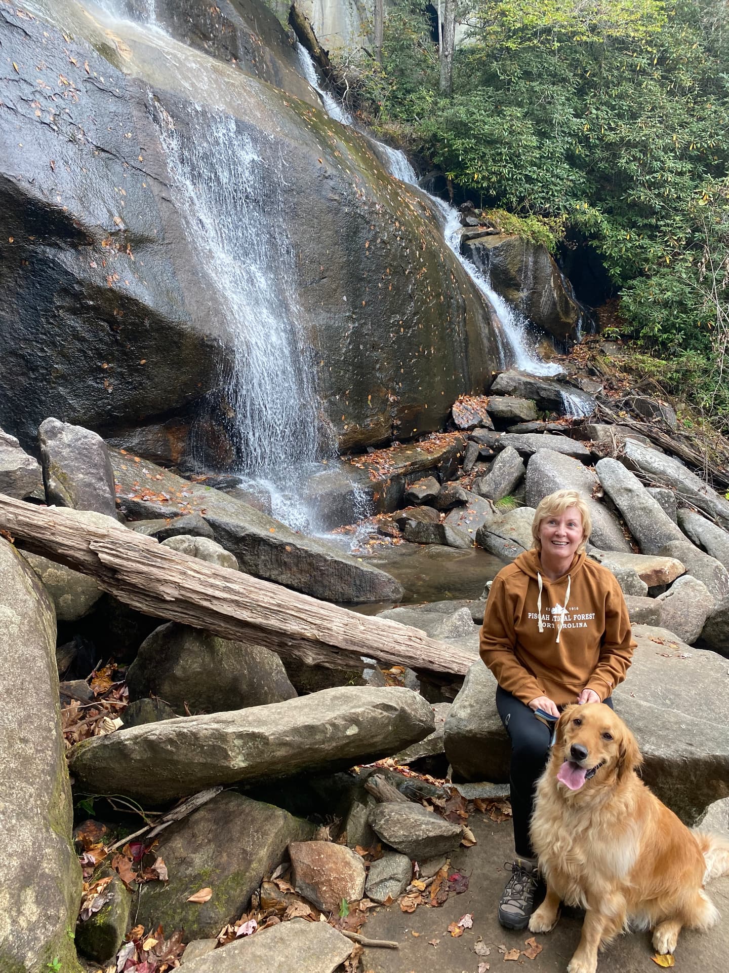 Karen and her dog sitting on rocks below a mountain waterfall