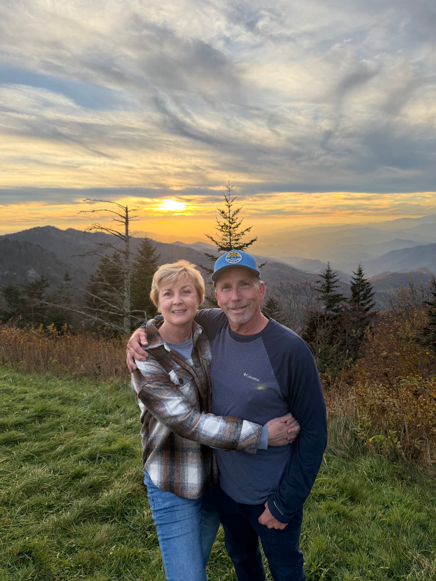 Karen and her husband hugging in front of a mountain sunset in Western North Carolina